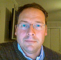 Man with short brown hair wearing glasses and a collared shirt 